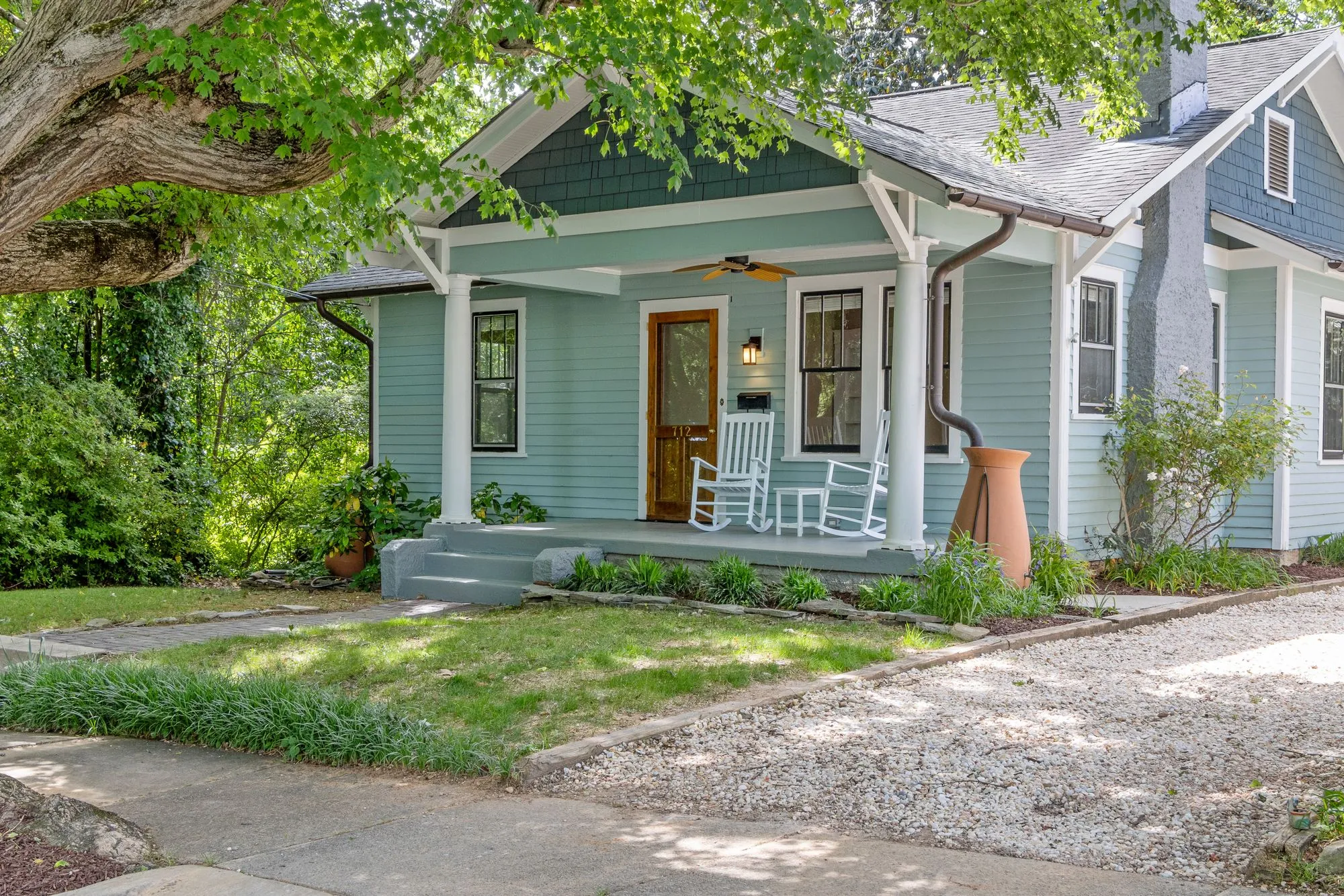 Sage-green bungalow with a white-pillared porch and rocking chairs behind a lawn