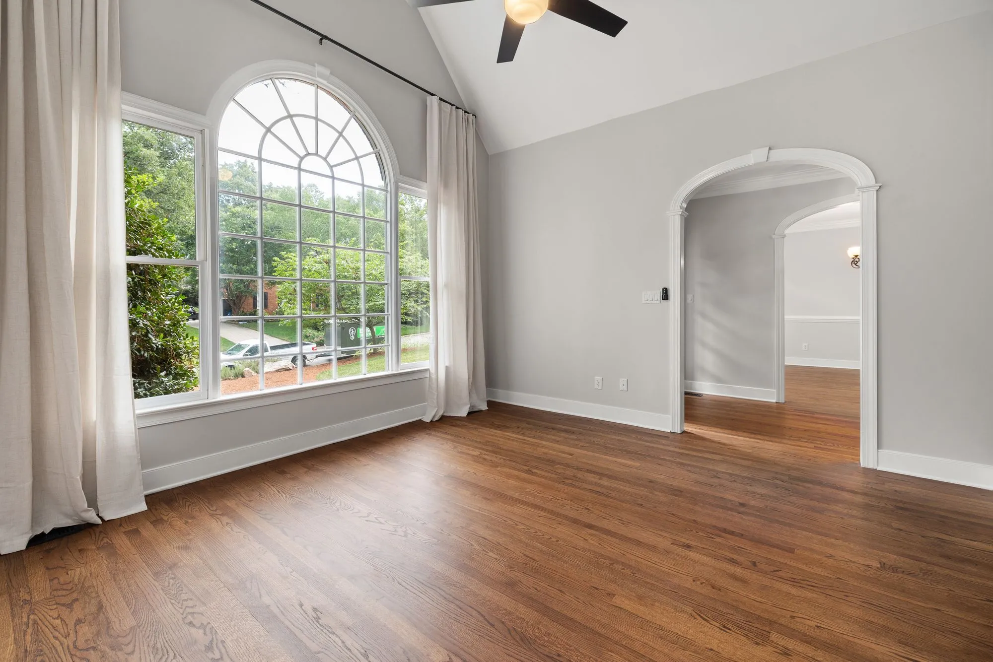 Empty living room with a tall arched window and warm wood floors