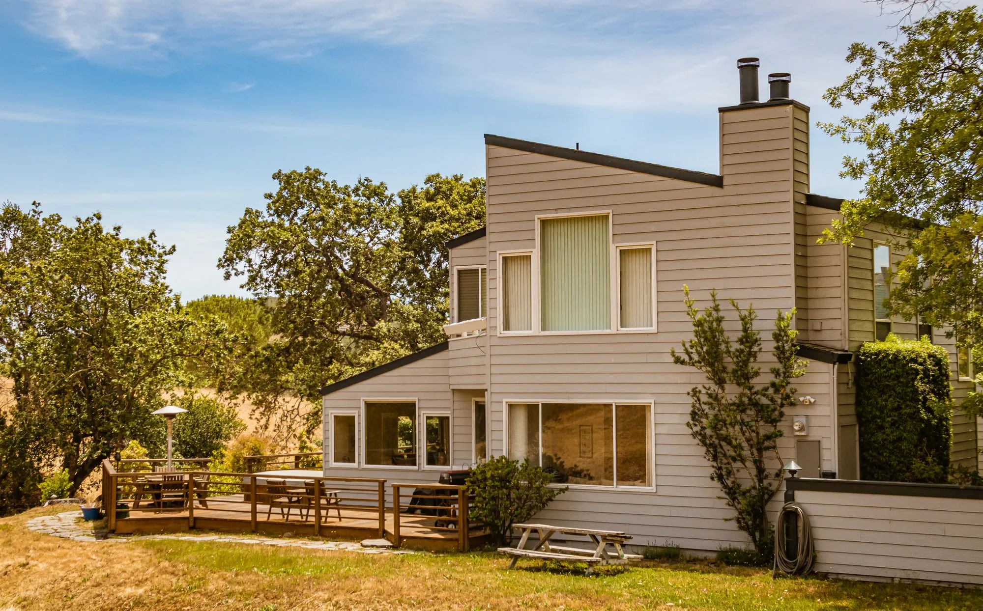 Mid-century house with tall windows and a wide deck among oak trees in evening sun