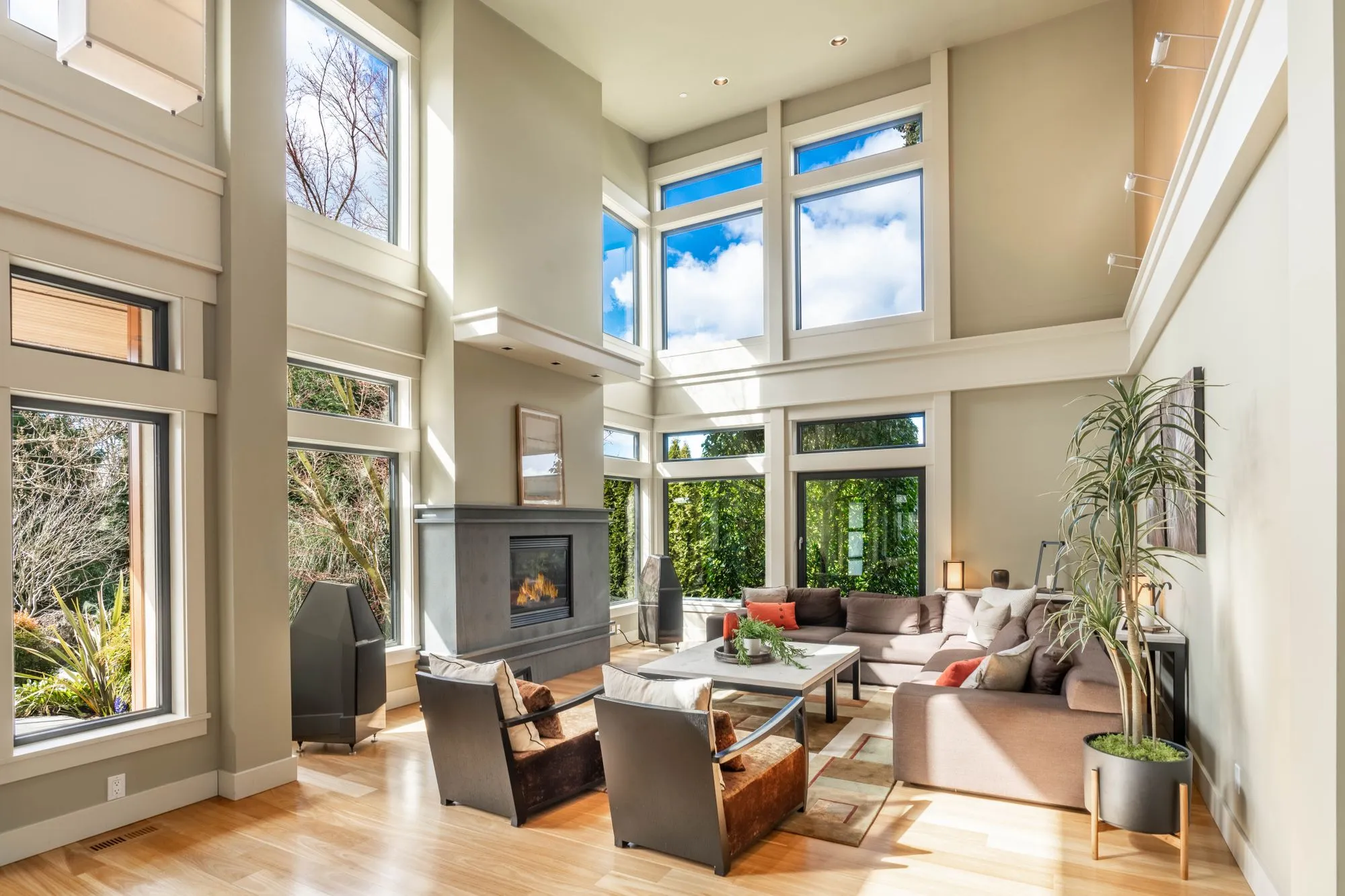 Bright two-story living room with tall windows, a fireplace and a staged sofa