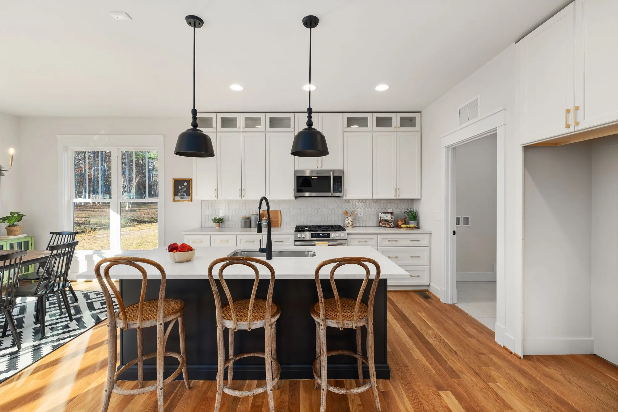 White kitchen with a navy island, three bentwood stools and pendant lights