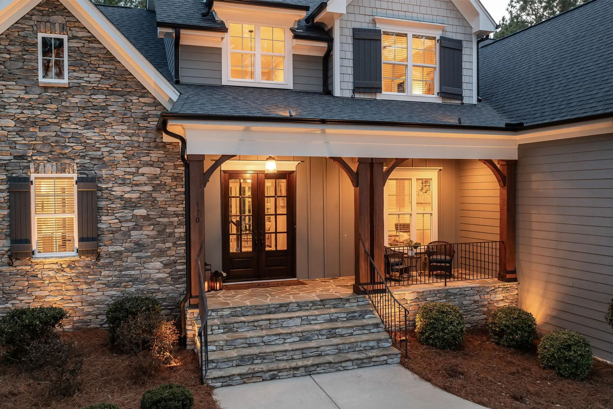 Stone-fronted house at dusk with a lit timber porch and stone steps